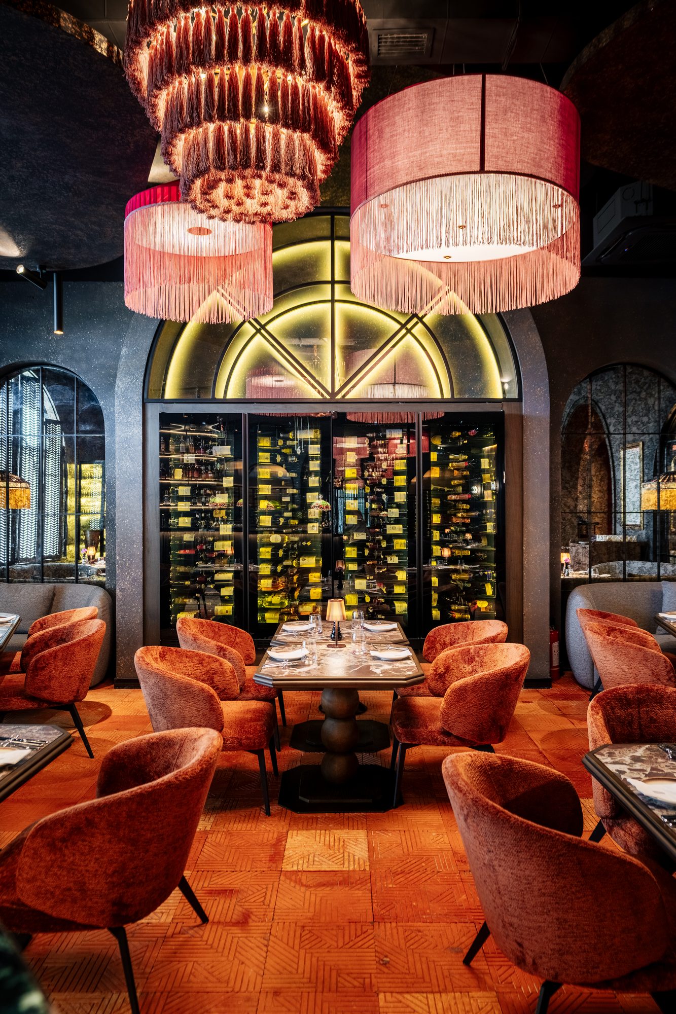 The upstairs lounge at Maison Rouge, pink fringed chandeliers over a lit wine wall